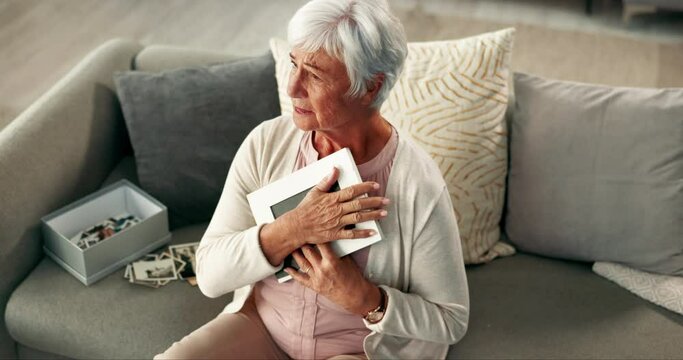 Senior woman, photo frame and sad on sofa with memory, thinking and mourning for grief in lounge. Elderly person, crying and depressed with hug, remember and picture on couch in living room at house