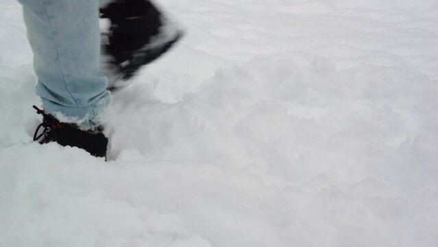 Male legs in black warm boots and blue denim trousers closeup. Man walks home from work through snowdrift in winter. White snow. Walk in park. Concept of loneliness, travel, wandering, loss. Lost