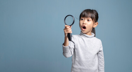 A little girl is holding a magnifying glass for studying.