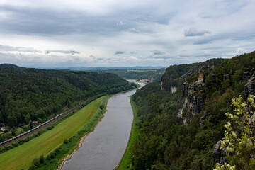 Fototapeta premium A river runs through a lush green valley. The sky is cloudy, and the trees are tall and green