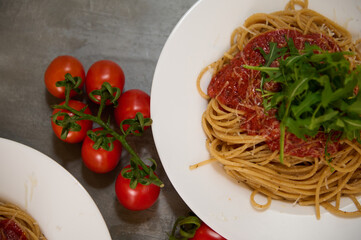 Food background with a branch of fresh ripe organic tomatoes cherry near plates of Italian pasta spaghetti a la Amatriciana with pancetta bacon and pecorino parmesan cheese. Italian cuisine. Top view.