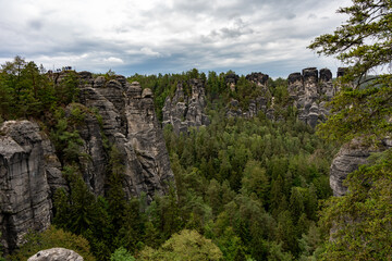 A mountain range with a forest in the background. The sky is cloudy and the trees are green