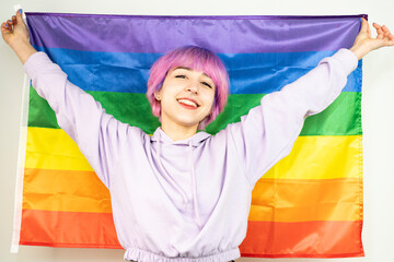 A woman with pink hair is holding a rainbow flag. She is smiling and she is happy. LGBT young woman...