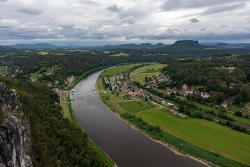 A river runs through a town with houses and a bridge. The sky is cloudy and the water is dark