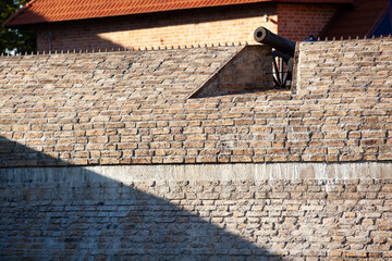 An ancient brick wall of the fortress. A large steel cannon on top of the wall. Background....