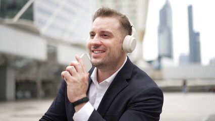 Professional business man listening headphone and using phone record voice while sitting at stair...