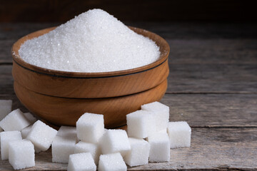Granulated sugar in a wooden cup, a scattering of refined sugar cubes.