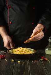 Adding dry pepper with a spoon in the cook hand to a plate of pasta. Chef at the kitchen table in a public house preparing a delicious lunch