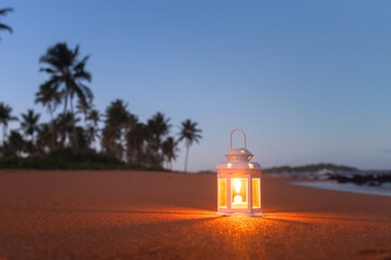 Candle lantern aglow, illuminating the sandy beach at dusk. The image conveys a sense of faith,...