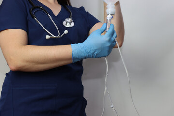 Health care professional wearing gloves holding and IV drip in the hands with a stethoscope in the neck and copy space in the right side of the photo 