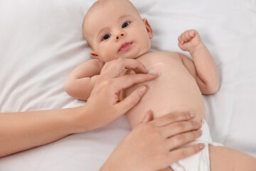 Woman applying body cream onto baby`s skin on bed, closeup