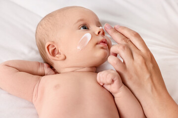 Woman applying cream onto baby`s face on bed, closeup