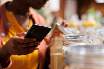 In this close-up image, black woman holds mobile device while checking out the items in the glass...