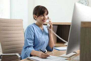 Smiling medical assistant talking by phone in office