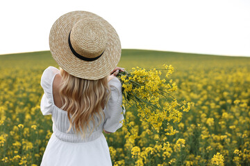 Young woman with straw hat in field on spring day, back view