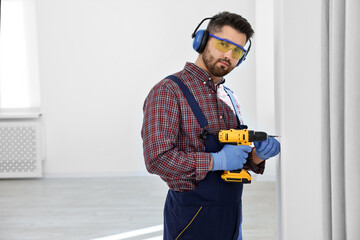 Young worker in uniform using electric drill indoors, space for text