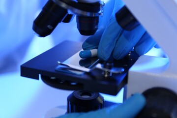 Scientist examining pill under microscope in laboratory, closeup