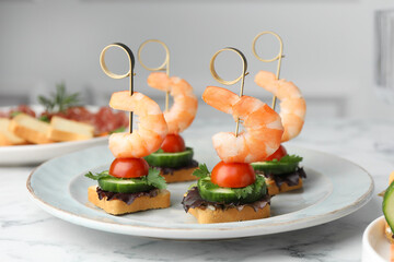 Tasty canapes with shrimps, cucumber, greens and tomatoes on white marble table, closeup