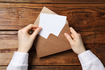 Woman taking card out of letter envelope at wooden table, top view