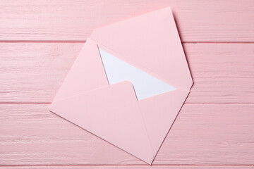 Letter envelope with card on pink wooden table, top view