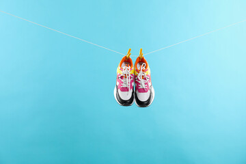 Stylish sneakers drying on washing line against light blue background