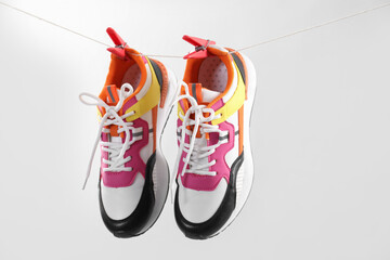 Stylish sneakers drying on washing line against light grey background