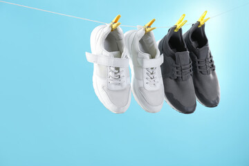 Different stylish sneakers drying on washing line against light blue background