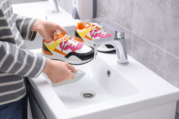 Woman washing stylish sneakers with brush in sink, closeup
