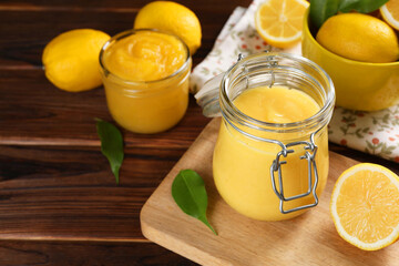 Delicious lemon curd in glass jars, fresh citrus fruits and green leaves on wooden table