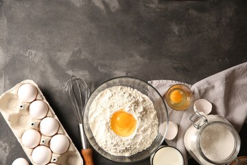 Making dough. Flour with egg yolk in bowl and other products on grey textured table, flat lay....