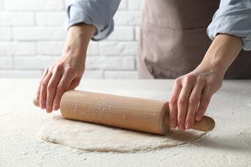 Woman rolling raw dough at table, closeup