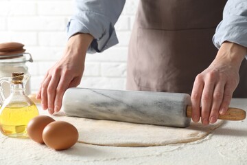 Woman rolling raw dough at table, closeup