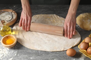 Woman rolling raw dough at grey table, closeup