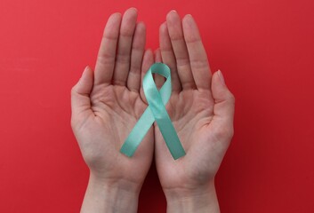 Woman holding turquoise awareness ribbon on red background, top view