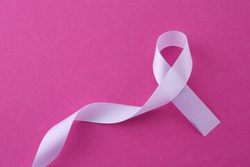 White awareness ribbon on pink background, top view