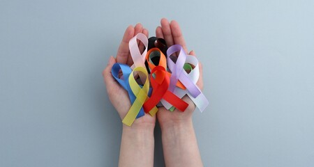 Woman with many colorful awareness ribbons on grey background, top view