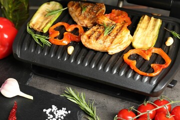 Electric grill with tasty meat, spices and vegetables on grey table
