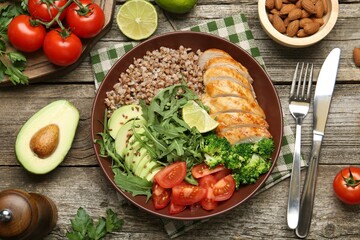 Healthy meal. Tasty products in bowl, ingredients and cutlery on wooden table, flat lay