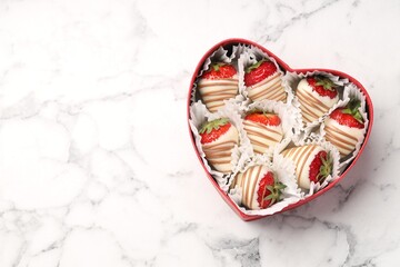 Heart shaped box with delicious chocolate covered strawberries on white marble table, top view. Space for text