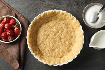 Making shortcrust pastry. Raw dough in baking dish, strawberries, sugar and milk on grey table, top...
