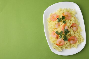 Delicious risotto with shrimps, lime and parsley on light green background, top view. Space for text