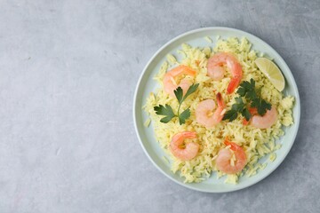 Delicious risotto with shrimps, lime and parsley on light grey table, top view. Space for text
