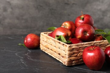 Fresh red apples and leaves in basket on dark grey table. Space for text