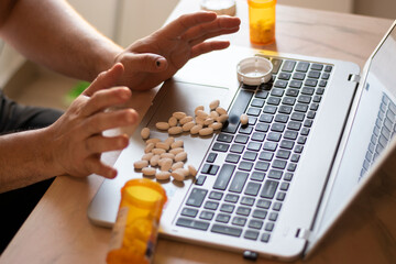 Person with addiction taking pills over his laptop with many pills around, desesperate