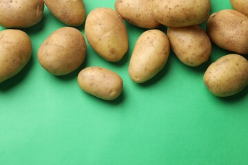 Fresh raw potatoes on green background, flat lay. Space for text