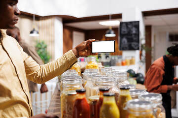 At eco friendly grocery shop African American male consumer holds a cell phone that displays an...