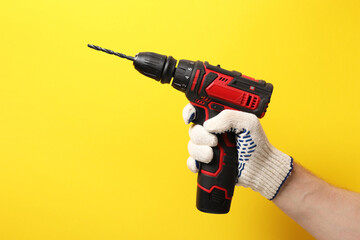 Handyman holding electric screwdriver on yellow background, closeup