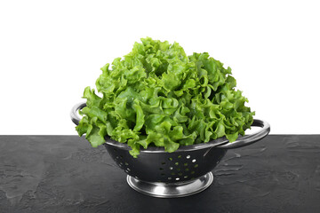 Metal colander with fresh lettuce on black textured table against white background