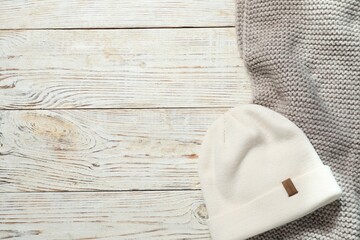 Gray knitted scarf and hat on wooden table, flat lay. Space for text