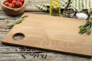 Cutting board, rosemary, oil and pepper on wooden table. Space for text